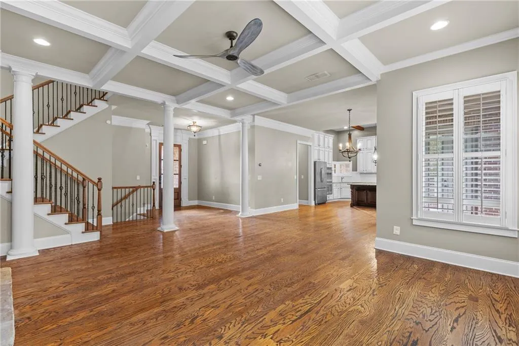 Unfurnished living room with ornate columns, coffered ceiling, beamed ceiling, dark wood-style floors, and a chandelier