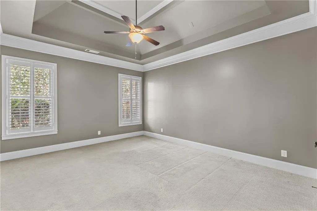 Empty room featuring ornamental molding, a ceiling fan, light colored carpet, and a raised ceiling