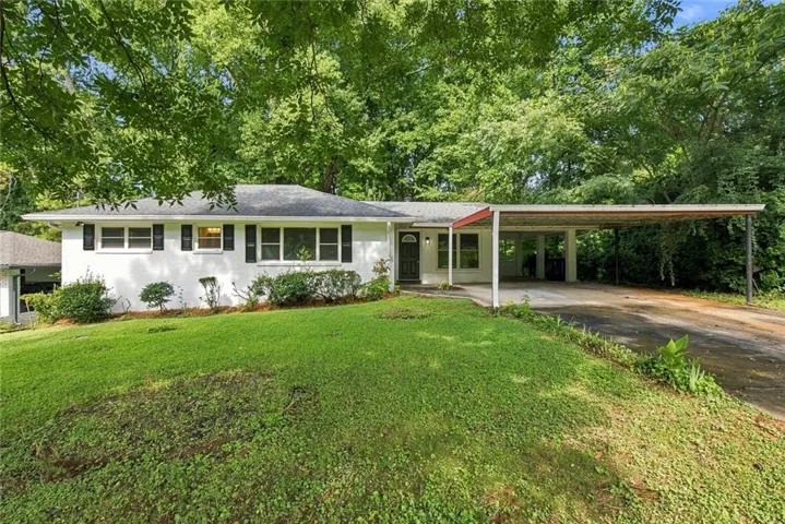 White brick exterior with a gray roof, black shutters, and a covered carport