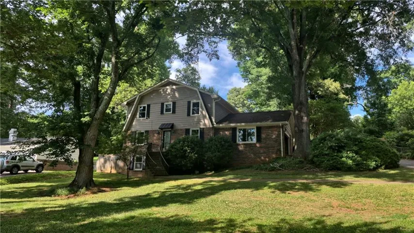 Gambrel roofline residence with a brick and siding exterior, featuring an elevated entrance and mature trees throughout the property