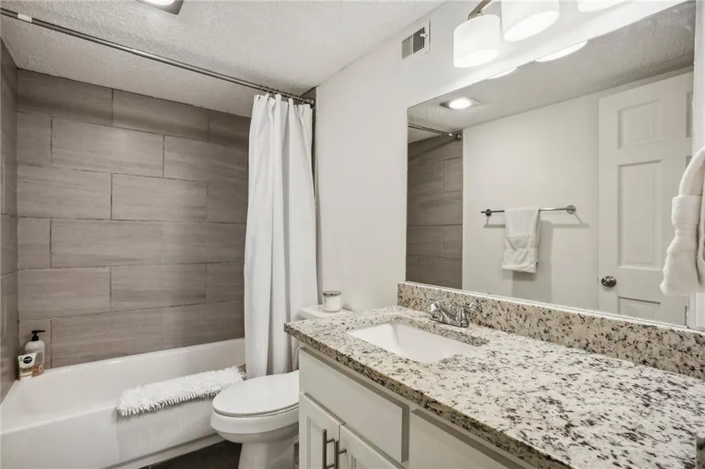 Secondary Bathroom with white cabinets and granite counters. Tiled tub/shower