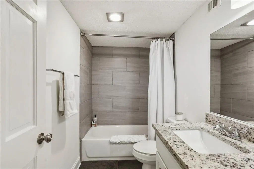 Bathroom featuring a textured ceiling, shower / bathtub combination with curtain, vanity, and dark tile patterned floors