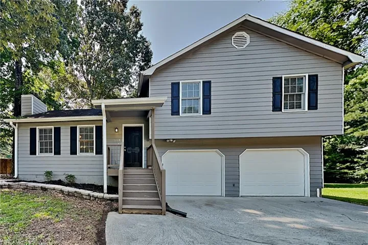 Split-level exterior featuring gray siding, a black front door, and a two-car garage with white doors