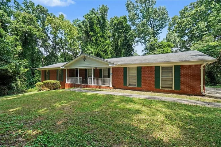 Brick ranch-style residence featuring a covered front porch with white railings, a front-facing gable, and green shutters complementing the red brick exterior