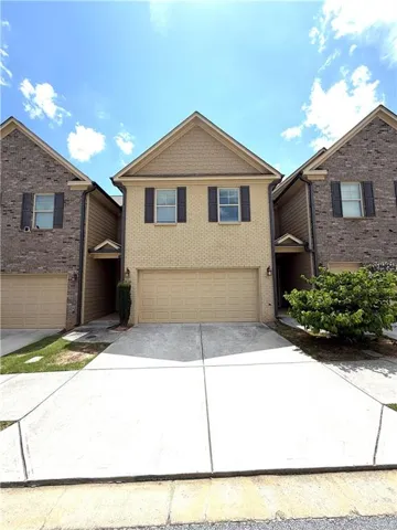 Two-story townhome featuring a beige brick facade with shake siding on the upper gable