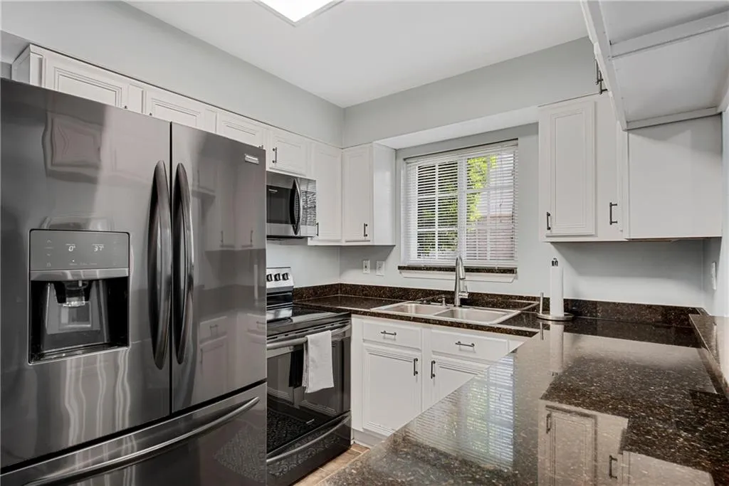 Kitchen featuring appliances with stainless steel finishes, sink, dark stone counters, and white cabinetry
