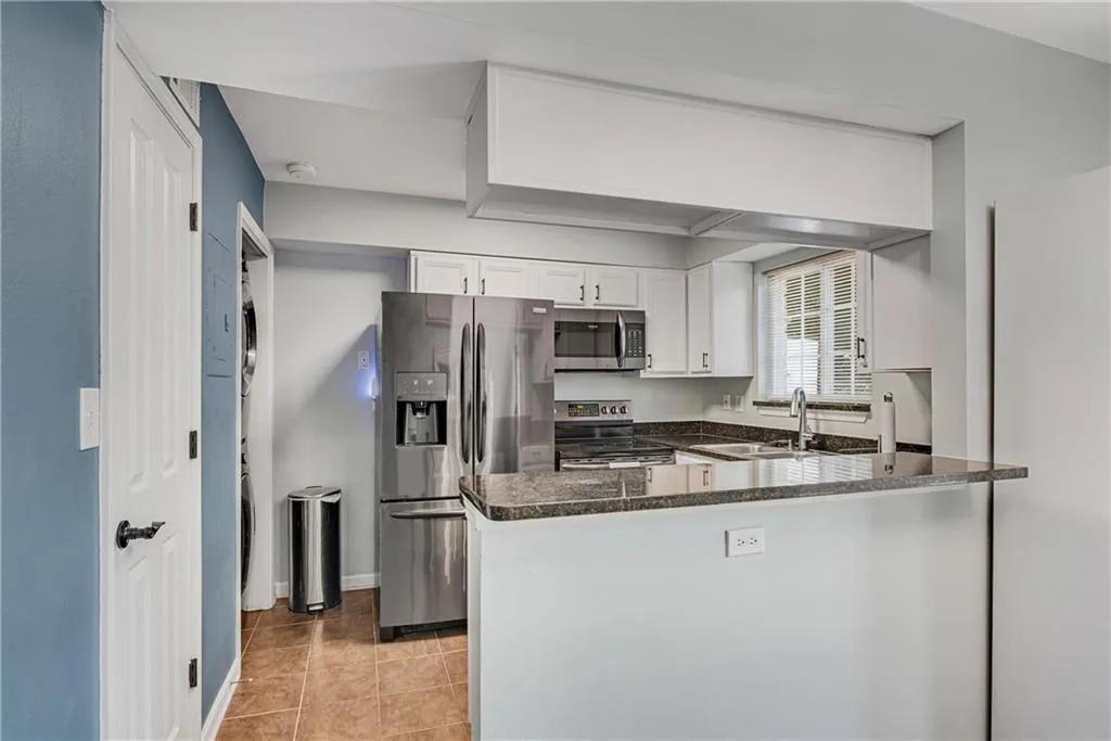 Kitchen with white cabinets, kitchen peninsula, stainless steel appliances, light tile floors, and dark stone counters