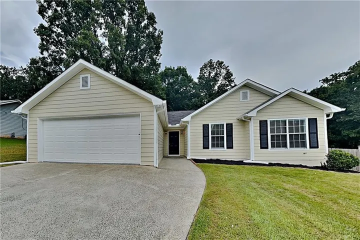 Single-story residence featuring light-colored siding, a two-car garage, dark shutters, a covered entry, and a concrete driveway