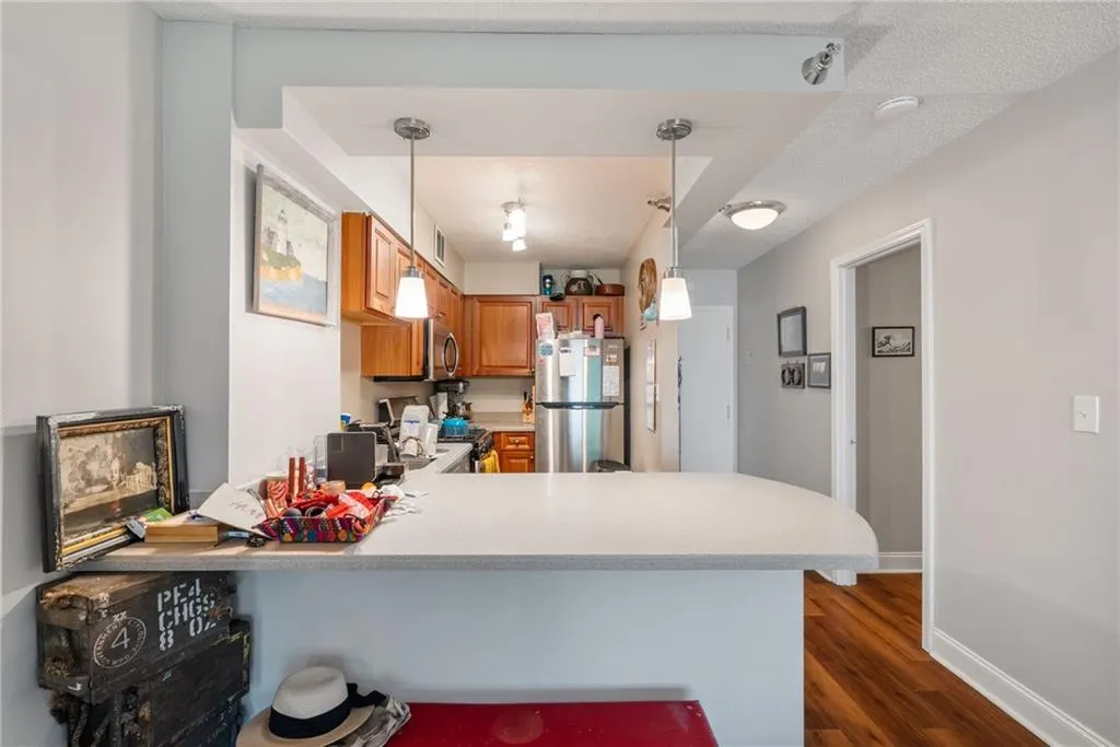 Kitchen with kitchen peninsula, hardwood / wood-style floors, decorative light fixtures, a textured ceiling, and stainless steel refrigerator