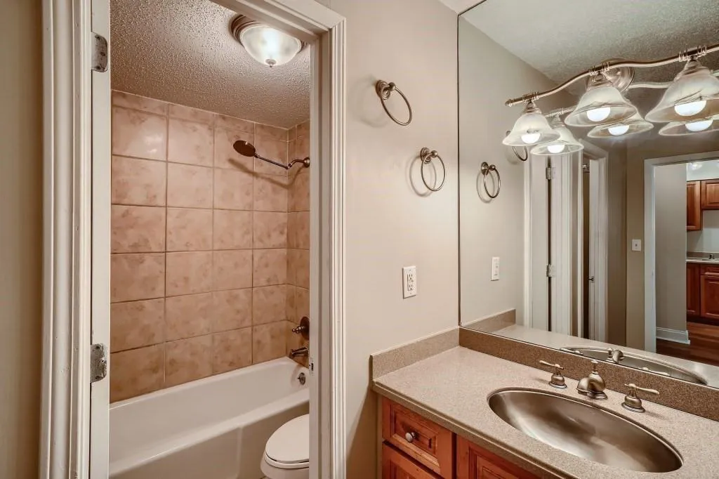 Full bathroom with tiled shower / bath, vanity, toilet, and a textured ceiling