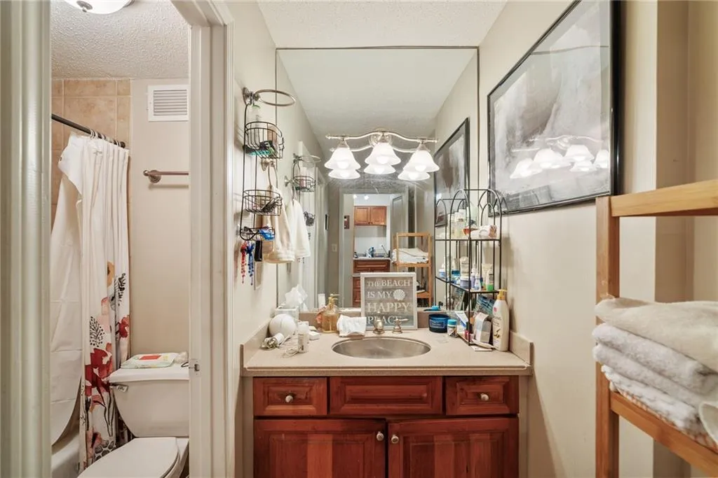 Full bathroom featuring shower / bathtub combination with curtain, vanity, toilet, and a textured ceiling