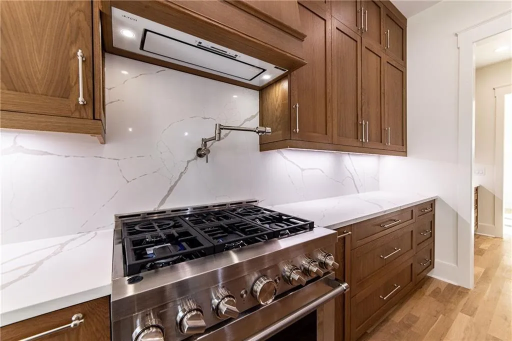 Kitchen with high end stainless steel range, brown cabinetry, light wood-style flooring, decorative backsplash, and extractor fan