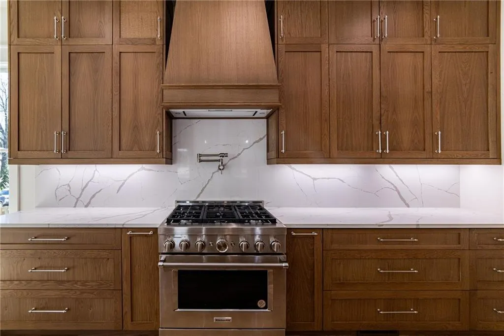 Kitchen with tasteful backsplash, high end stainless steel range, custom exhaust hood, and brown cabinets