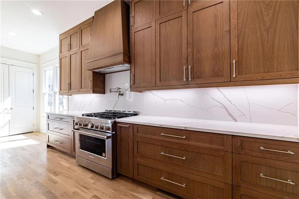 Kitchen featuring premium range hood, decorative backsplash, stainless steel stove, light stone counters, and light wood-style floors