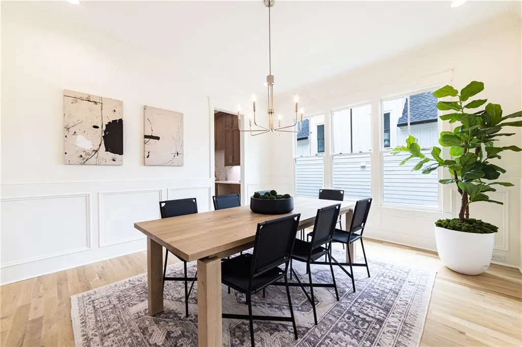 Dining area featuring a chandelier, a decorative wall, ornamental molding, light wood-type flooring, and a wainscoted wall