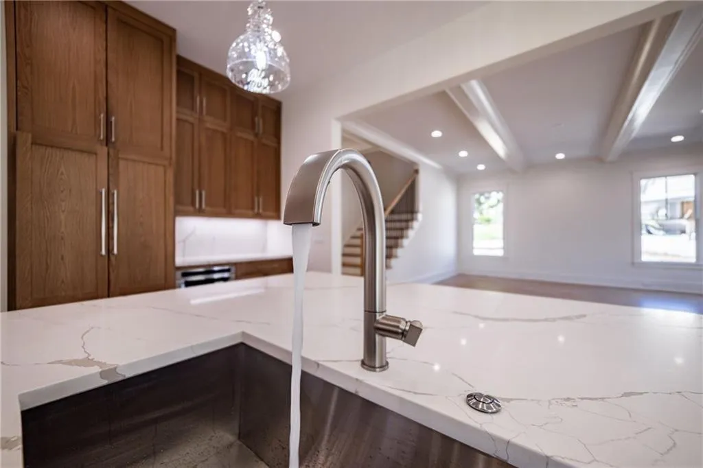 Details featuring light stone countertops, brown cabinets, recessed lighting, beam ceiling, and pendant lighting