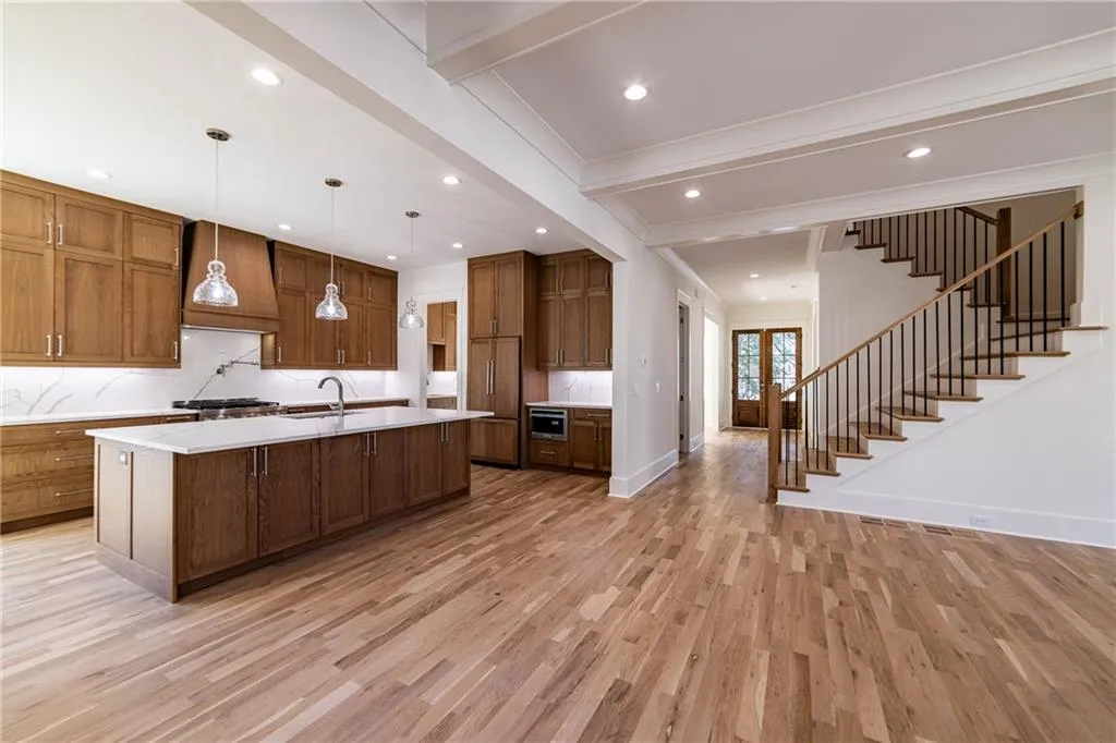 Kitchen featuring light countertops, beam ceiling, light wood-type flooring, custom range hood, and a large island with sink