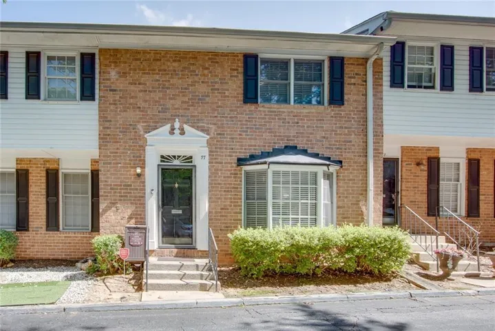 Brick townhome facade featuring a prominent bay window with white blinds, dark louvered shutters, and a white decorative door surround