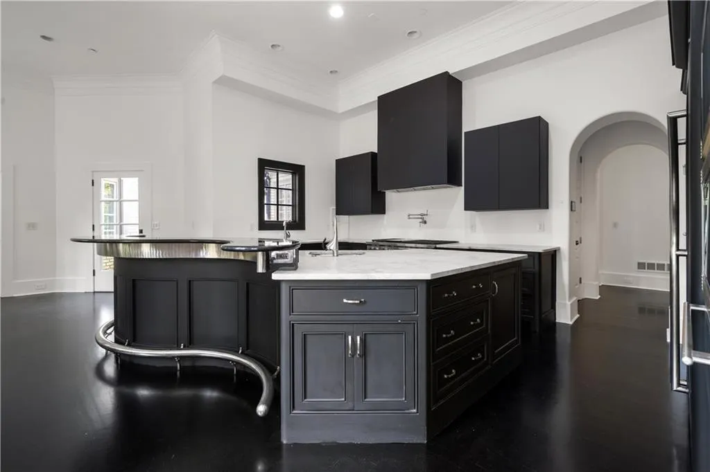 Kitchen with dark cabinets, ornamental molding, a large island with sink, arched walkways, and light stone countertops