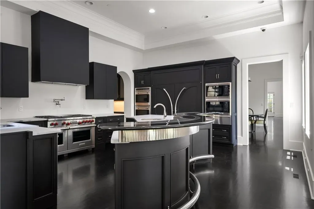 Kitchen with dark cabinets, crown molding, stainless steel appliances, arched walkways, and a center island with sink