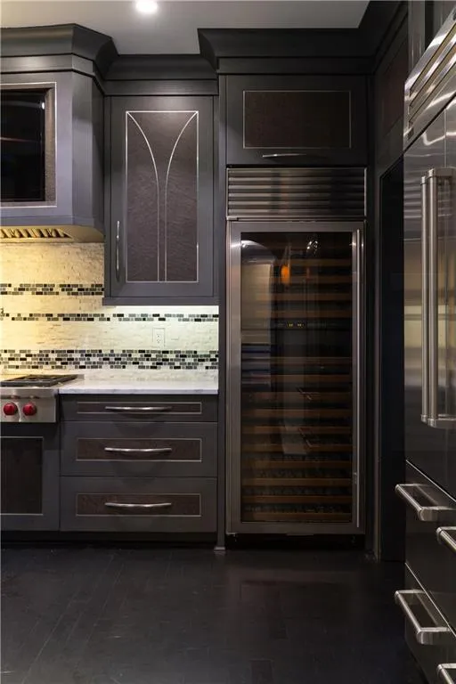 Kitchen with wine cooler, tasteful backsplash, light stone countertops, stainless steel appliances, and ventilation hood