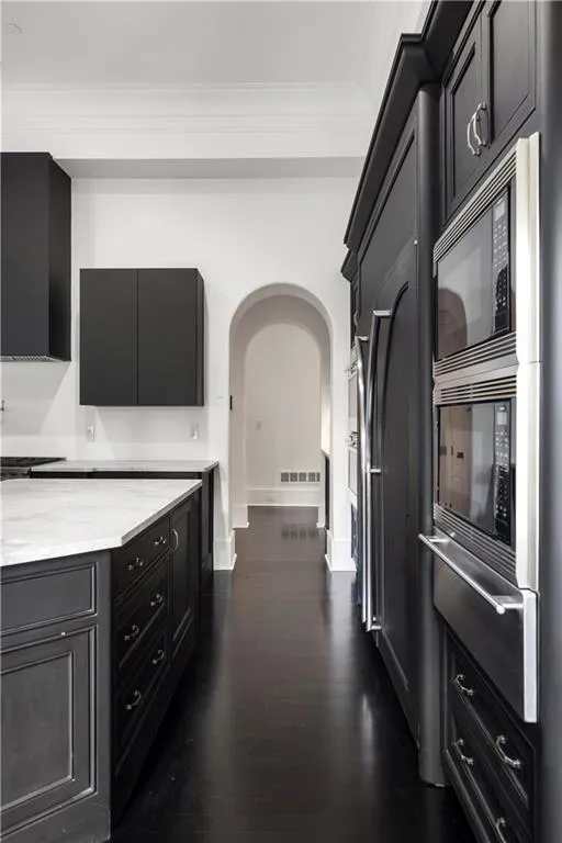 Kitchen with dark cabinets, dark wood-style floors, a warming drawer, light stone countertops, and ornamental molding