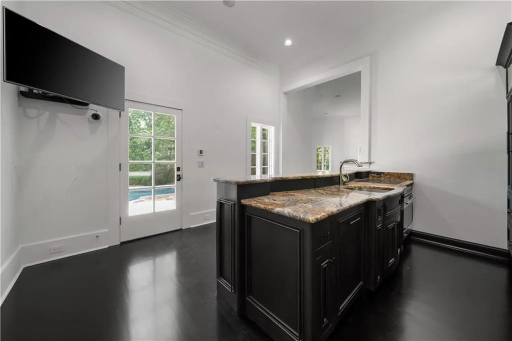 Kitchen featuring dark cabinets, a peninsula, light stone counters, ornamental molding, and dark wood-style flooring