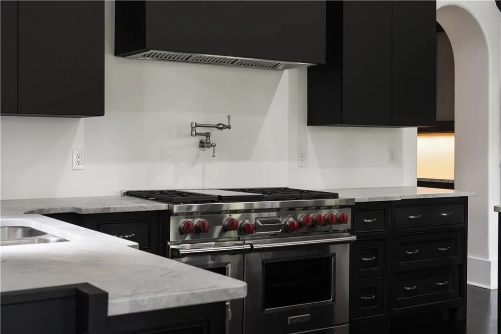 Kitchen with dark cabinetry, range with two ovens, and light stone countertops