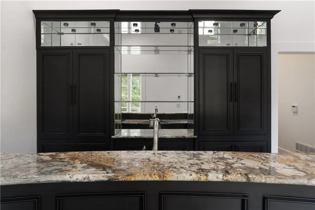 Kitchen featuring dark cabinetry, light stone counters, and glass insert cabinets