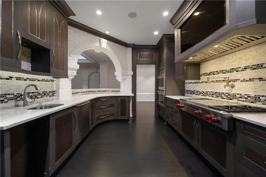 Kitchen featuring decorative backsplash, light stone counters, stainless steel appliances, dark brown cabinetry, and exhaust hood