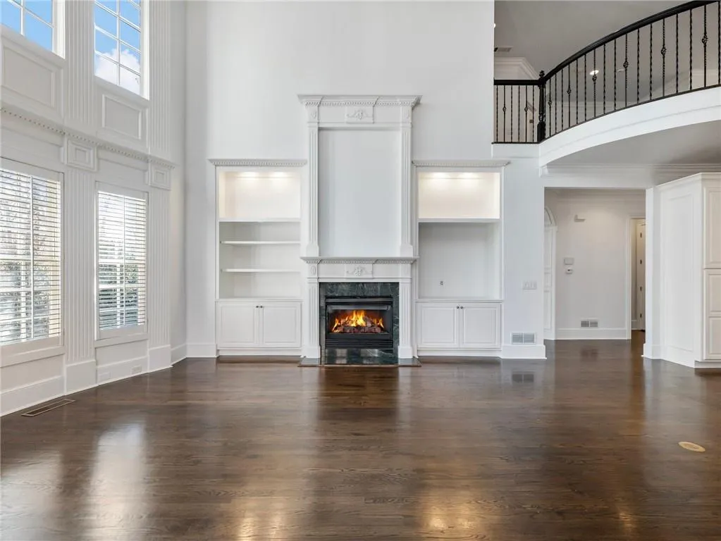 Great room room with crown molding, built in features, dark wood-type flooring, a towering ceiling, and a premium fireplace.