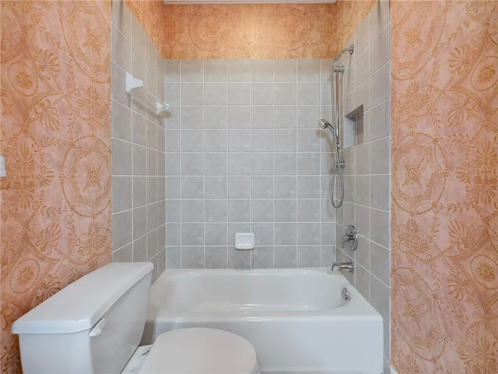 Bathroom with tiled shower / bath combo and toilet.