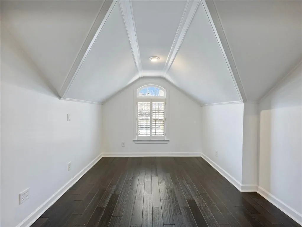 Additional living space featuring vaulted ceiling and dark wood flooring.