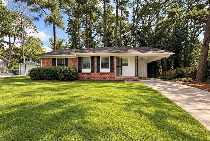 Brick and white siding exterior with a carport, mature landscaping, and a manicured lawn