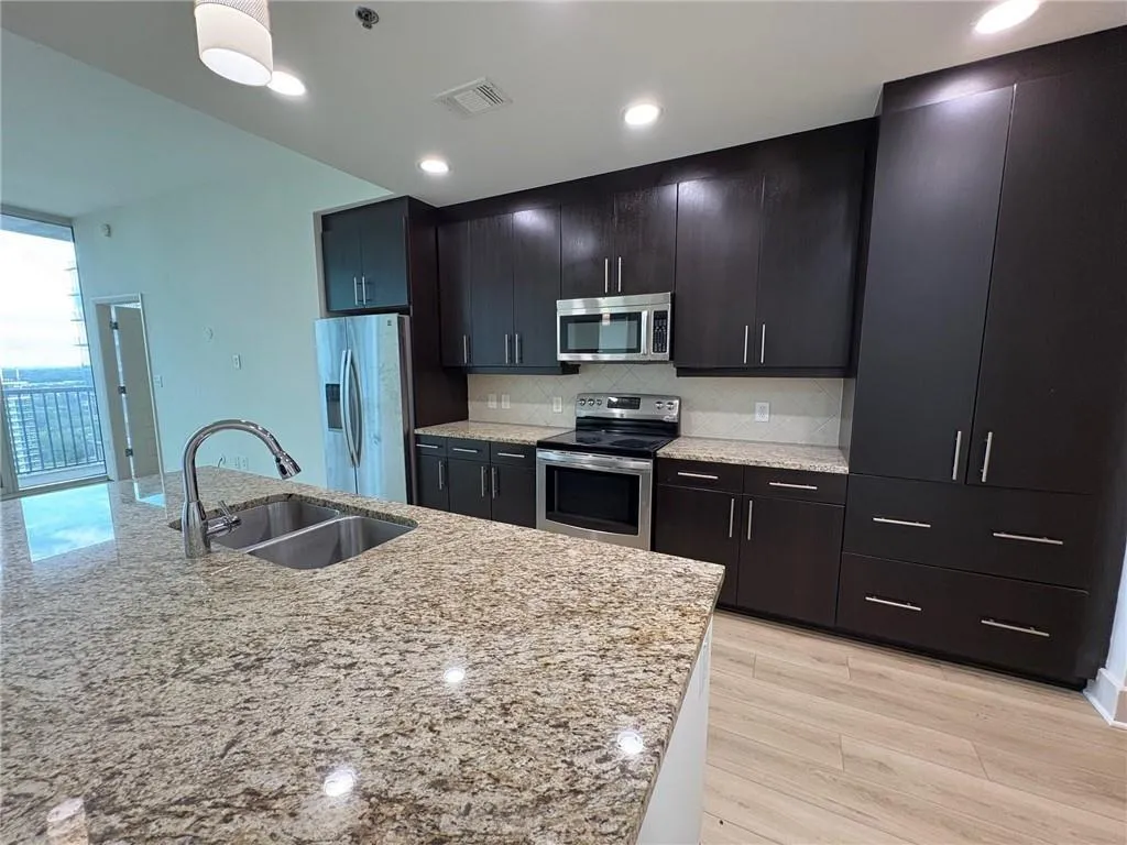 Kitchen with stainless steel appliances, tasteful backsplash, light stone counters, light wood-style floors, and recessed lighting