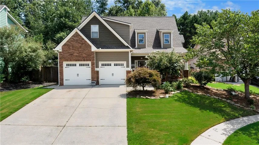 Two-story residence featuring a brick and siding exterior, a two-car garage with white paneled doors, a prominent dormer window, an asphalt shingle roof, and a concrete driveway