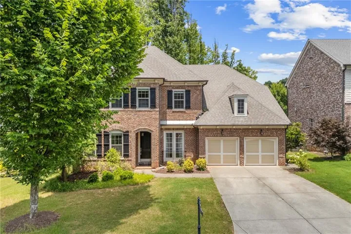 Traditional brick facade residence featuring a two-car garage, mature landscaping, a concrete driveway, and dormer windows