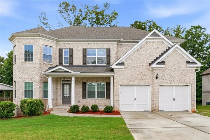 Cream brick facade featuring a covered front entry, bay windows, dark shutters, and a two-car garage
