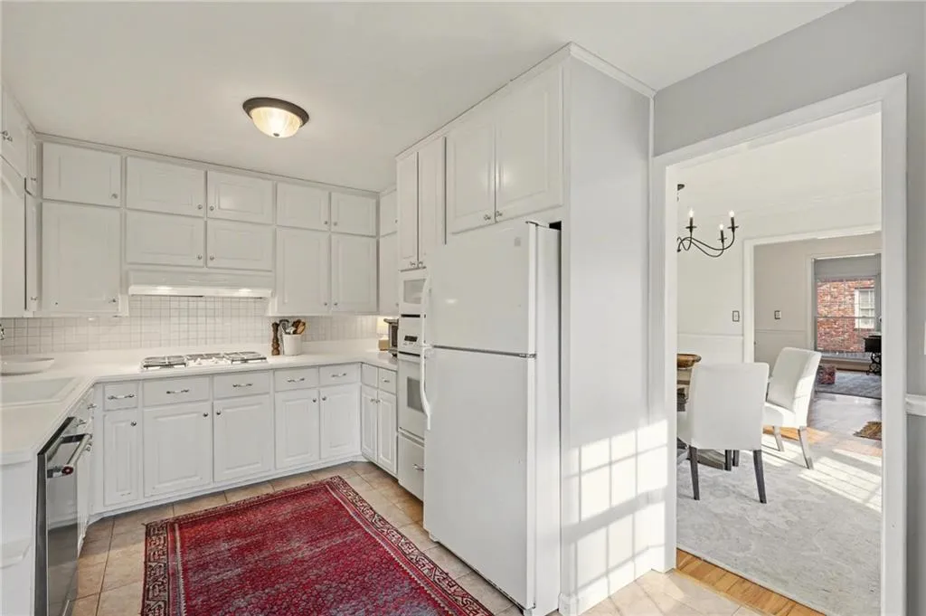 Kitchen featuring white appliances, light countertops, white cabinets, a chandelier, and tasteful backsplash