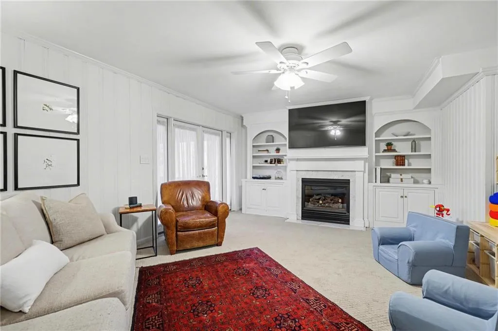 Living room with a fireplace with flush hearth, built in features, carpet floors, and ornamental molding