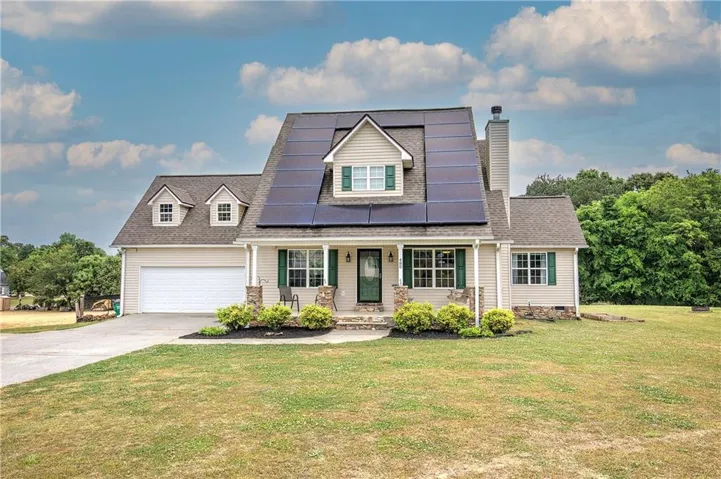 Two-story residence featuring light-colored siding, a covered front porch with stone-clad columns, and a prominent solar panel array on the roof