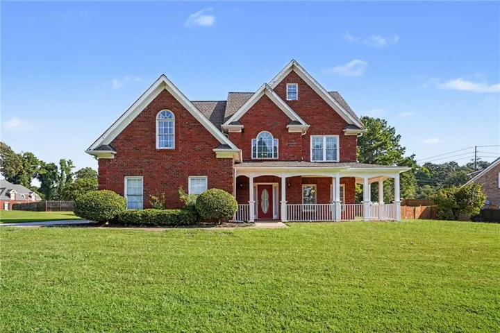 Red brick exterior with white trim, featuring multiple gables, a covered front porch with white columns, and a manicured front lawn