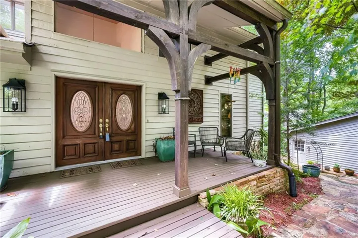 Front entry featuring double wooden doors with decorative oval glass inserts, flanking wall-mounted lanterns, and a large covered porch with exposed timber framing