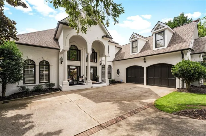 Stucco exterior with arched entry, prominent columns, dormer windows, a two-car garage, and a concrete driveway with brick detailing
