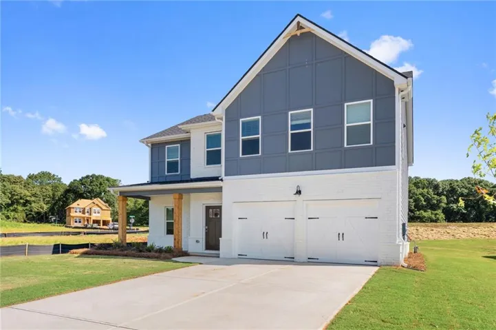 Contemporary two-story residence featuring a white brick and gray board-and-batten facade, a covered front porch with natural wood columns, a two-car garage with carriage-style doors, and a concrete driveway