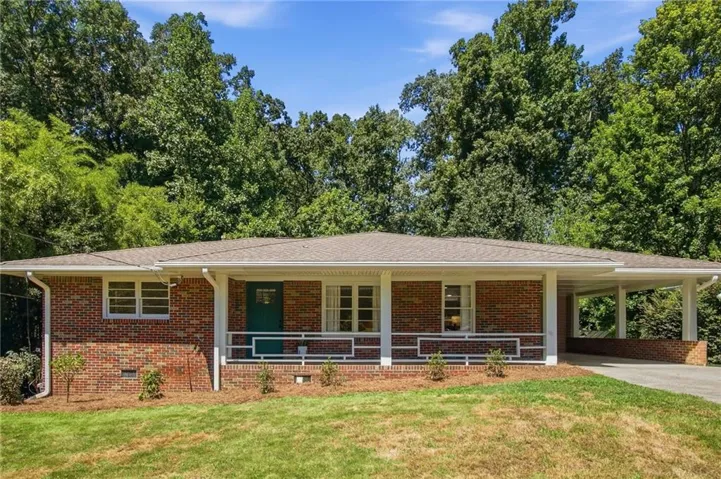Classic brick ranch home with a welcoming front facade featuring a covered porch, multiple windows providing natural light, and a carport extension