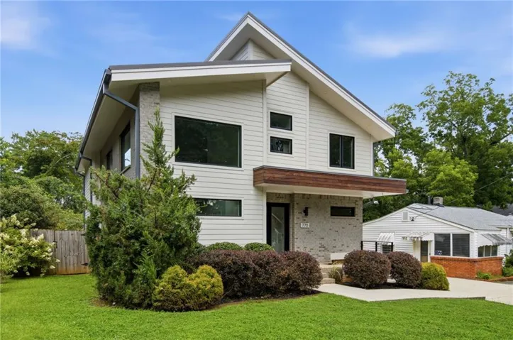 Modern two-story residence featuring clean-lined white exterior siding, substantial multi-pane windows with dark frames, and a striking wood-finish accent panel