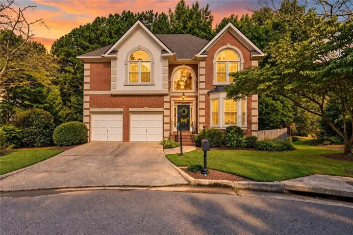 Traditional-style brick residence featuring a two-car garage, arched windows, and a landscaped front yard with mature trees