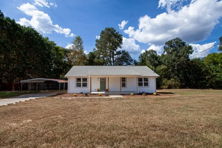White exterior, covered carport, gravel driveway, gray shingle roof, established trees