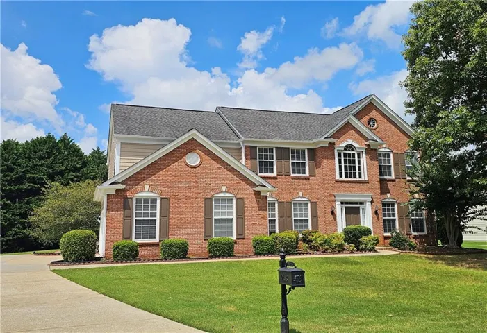 Traditional brick exterior with siding accents, gabled rooflines, multiple windows with shutters, and a concrete driveway